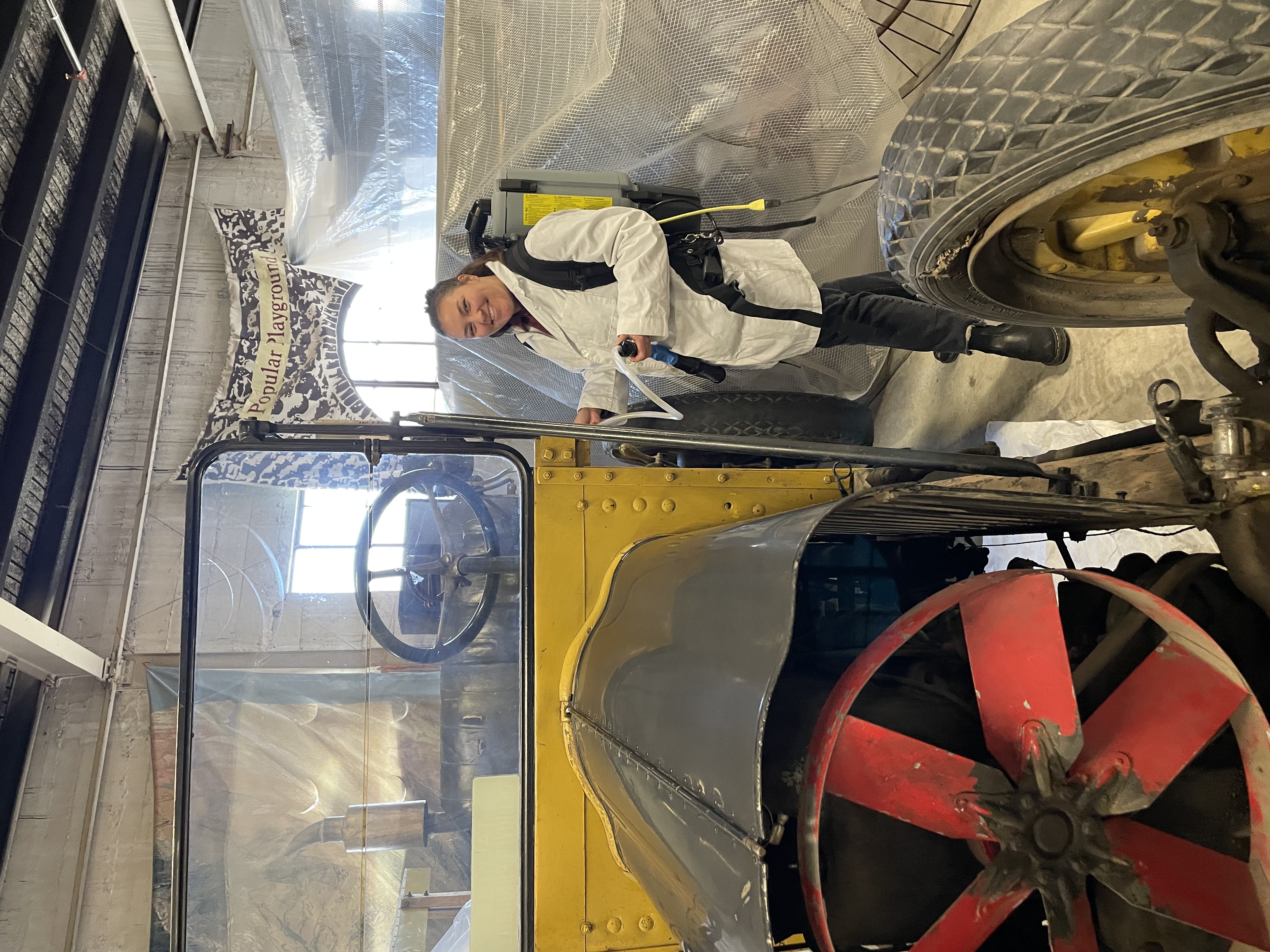 Museum technician vacuuming historic vehicle with backpack vacuum.