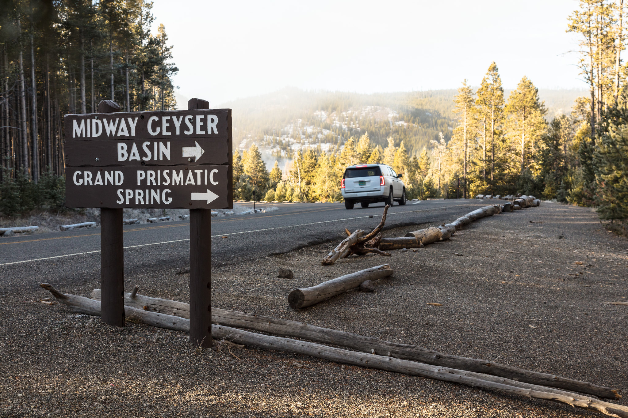 A vehicle driving by a wooden sign with the words Grand Prismatic Springs