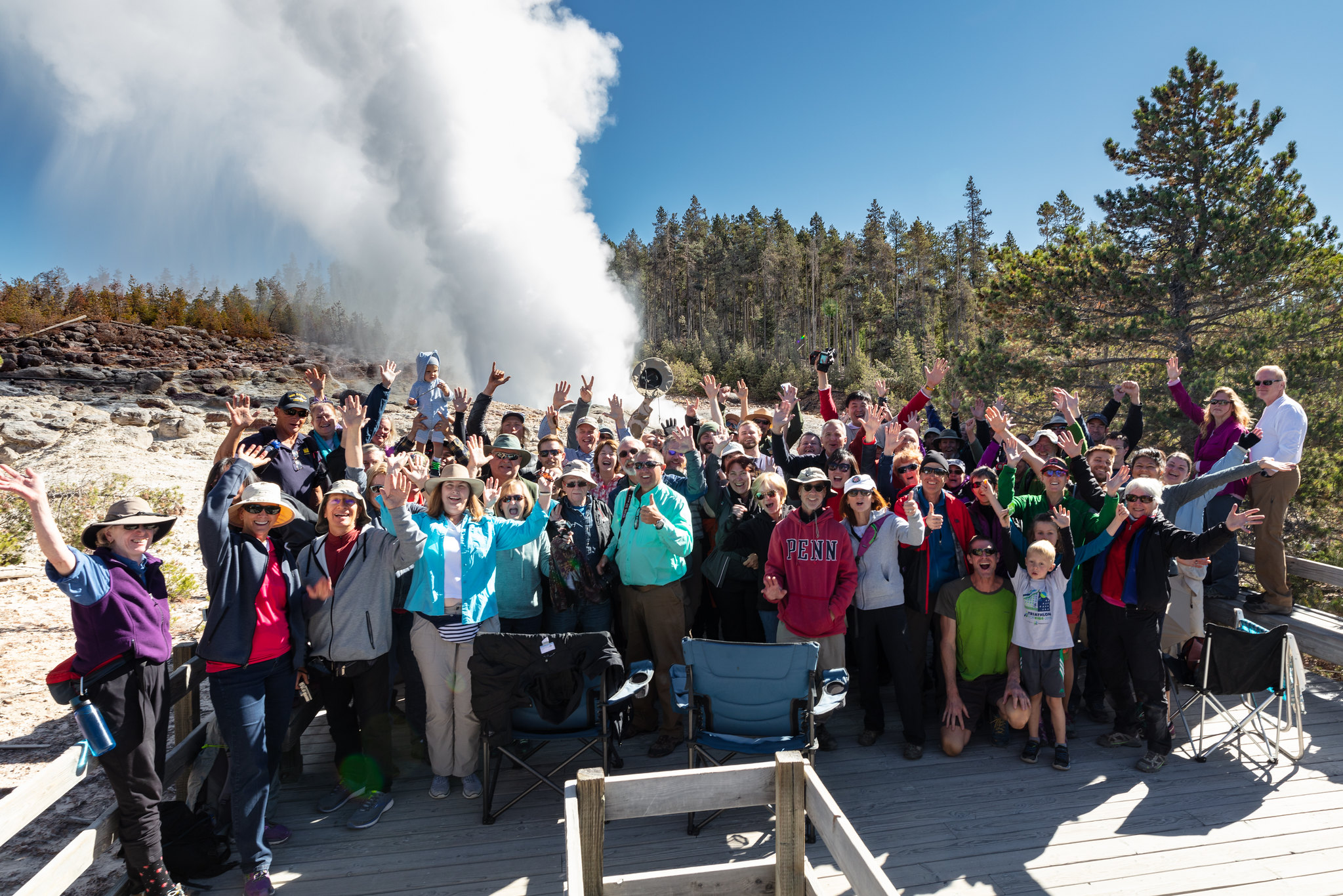 visitors waving in front of geyser