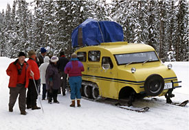 Visitors stand in the snowy landscape by a snowcoach.