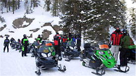 Group of winter visitors getting ready to take off on snowmobiles.