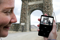 Visitor standing by Roosevelt arch looking at ipod video about the arch!