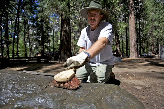 A volunteer scrubs the marker stone of Forest Townsley, Chief Ranger in Yosemite from 1916 until his death in 1943.