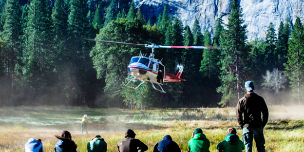 Helicopter lands in a meadow as people look on