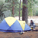 Person kneeling next to tent in a campground. Photo by Ray Santos.