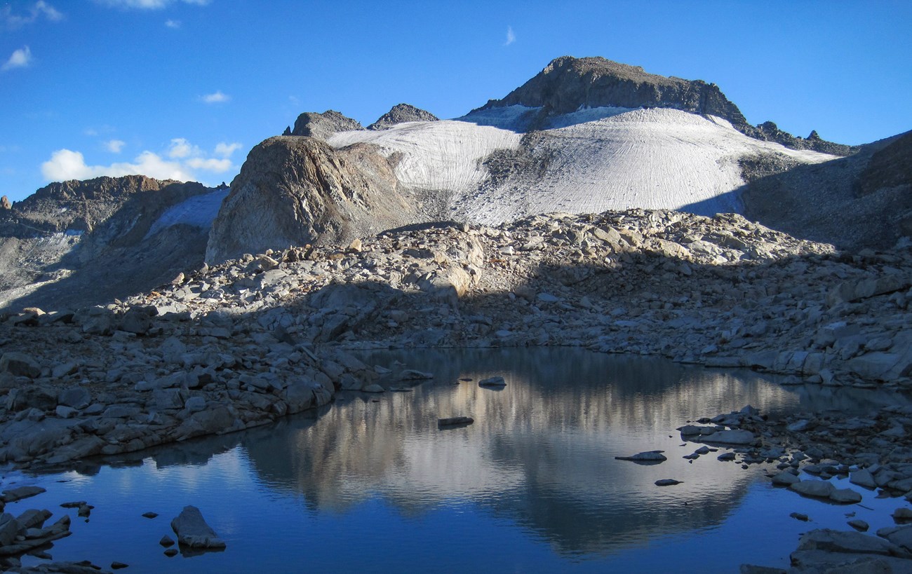 Ice sheet rests on rocky slope above alpine lake