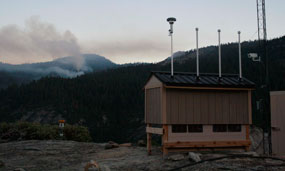 An air quality monitoring station sits on top of a mountain with a fire behind it
