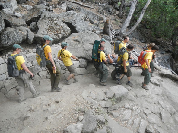 Rescuers wheel a litter with patient down the trail