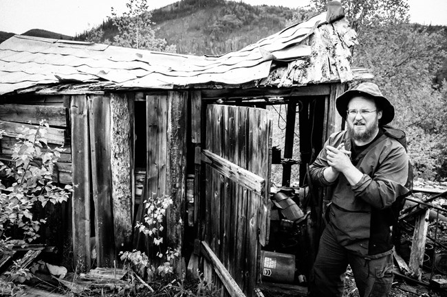 black and white photograph of park historian in front of a historic cabin