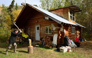 A visitor splits wood in front of the Smith public use cabin