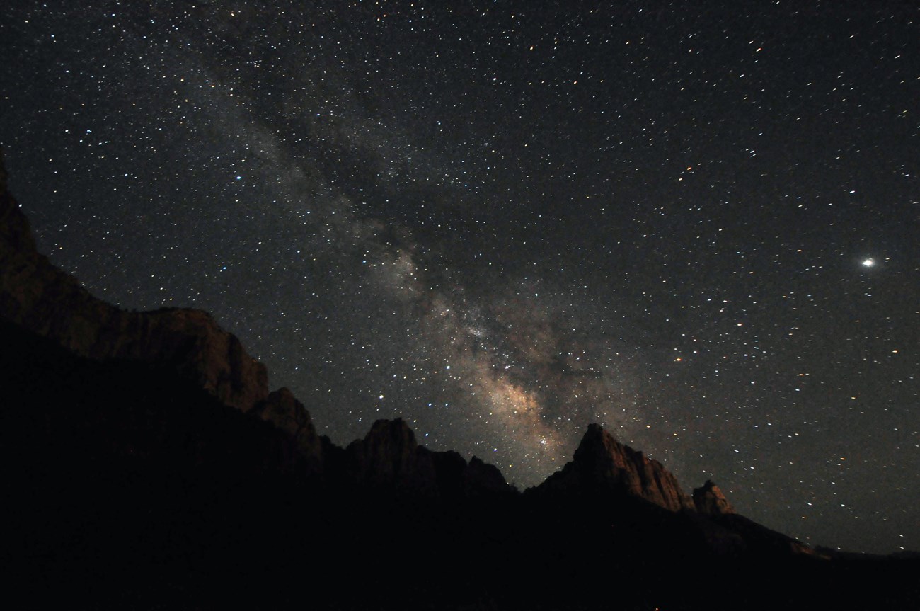 Dark Sandstone tower, named Watchman, looms under the night sky. Stars dot the night sky as the Milky Way spans the sky