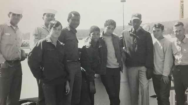 Men in work uniforms lean against the side of a boat