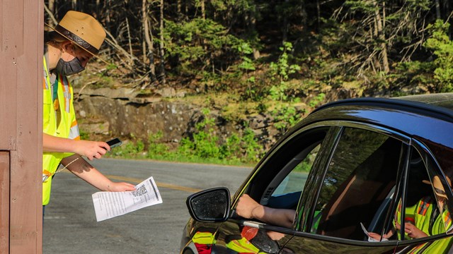 Ranger leans out of booth window to scan a device held by a driver of a vehicle.