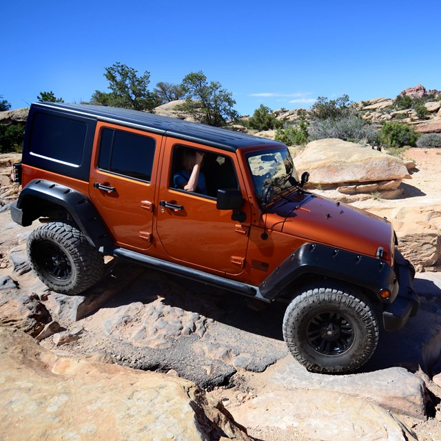 an orange Jeep driving over a steep, rocky surface