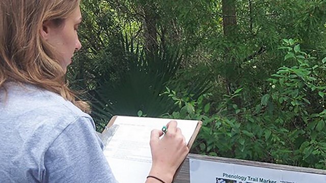 Women making notes on a clipboard near plants