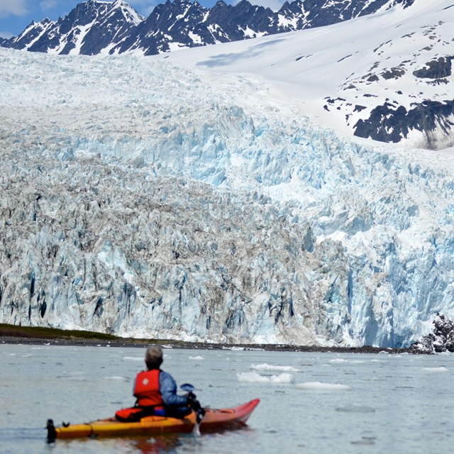 A person kayaking in front of a tidewater glacier.
