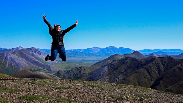 woman jumping on top of a mountain