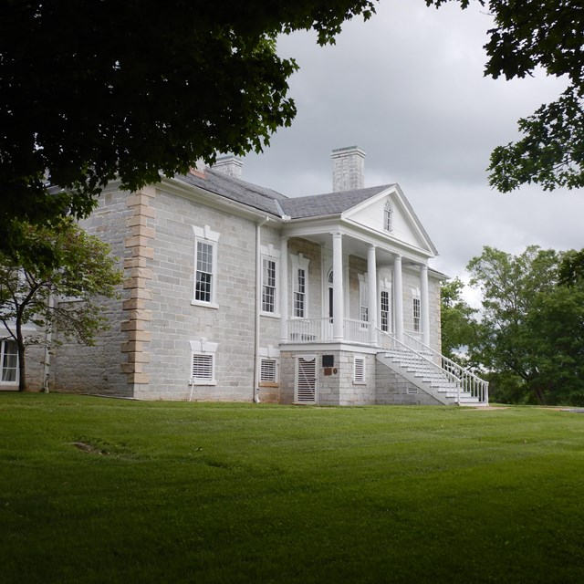 Color photograph of a large stone house surrounded by trees.