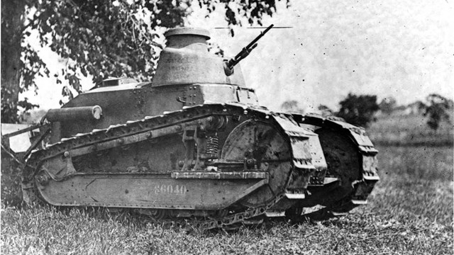 An army tank sits under a tree.