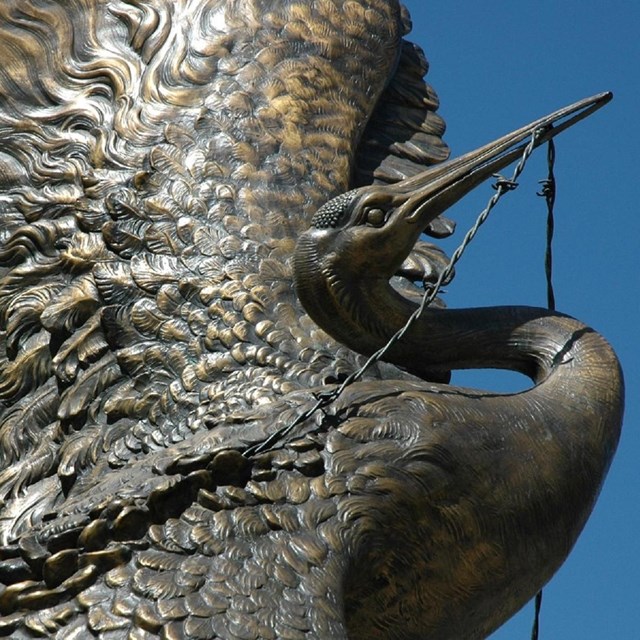 statue of a crane with raised wings freeing itself from barbed wire