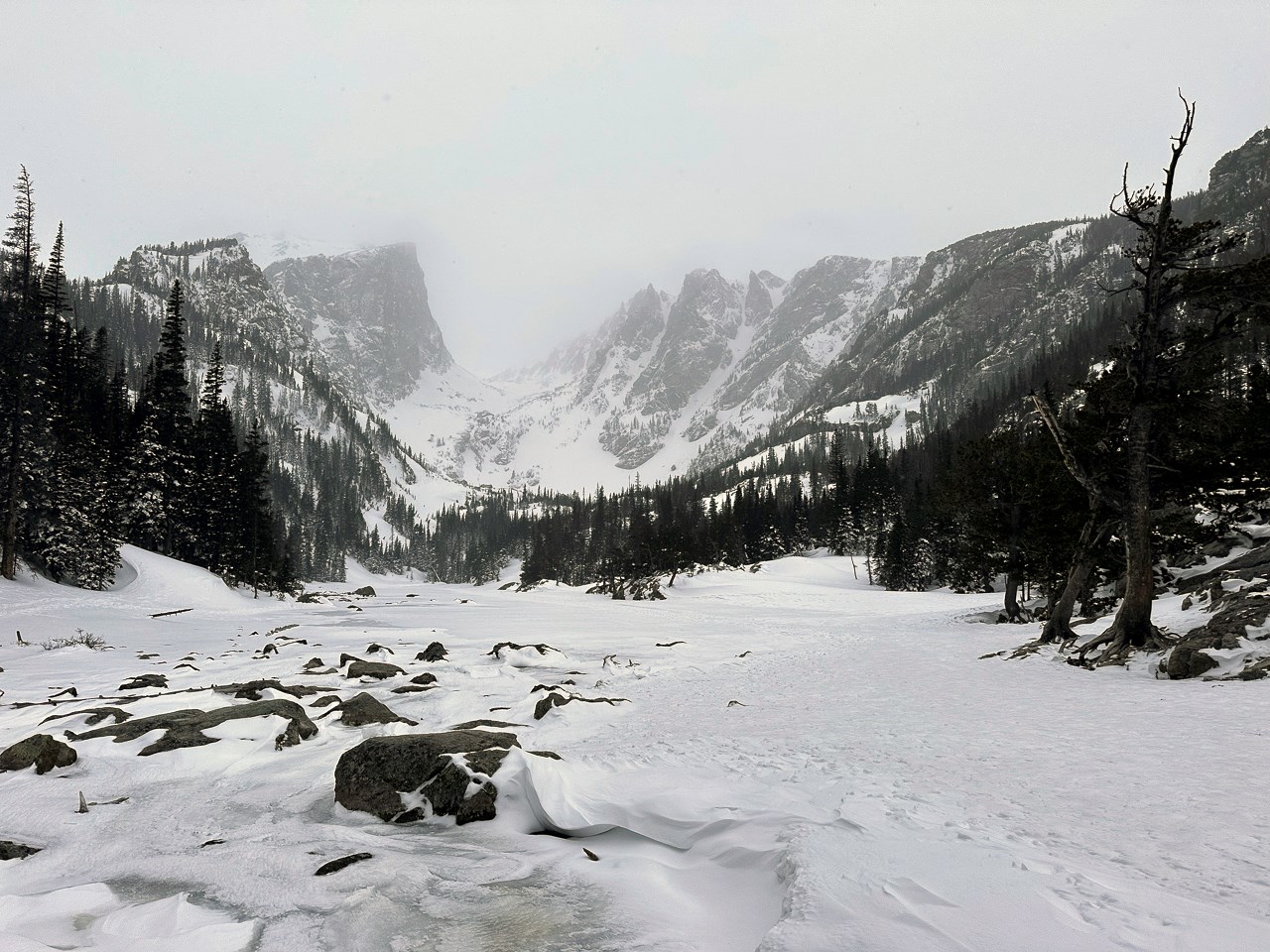Very snowy mountains and snowy Dream Lake. Ice is melting on Dream Lake. NPS photo taken May 9, 2024