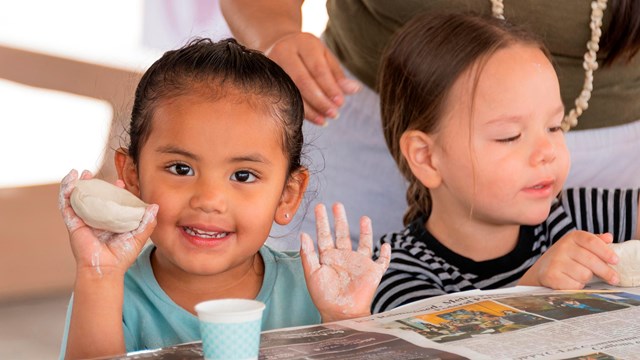 A  smiling student holds up a clay pinch pot. 