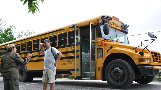 Ranger stands near school bus delivering students for field trip.