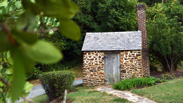 A tiny stone cabin surrounded by green leaves