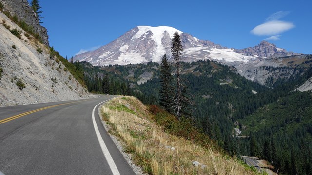 A road curves up the side of a valley towards Mount Rainier.