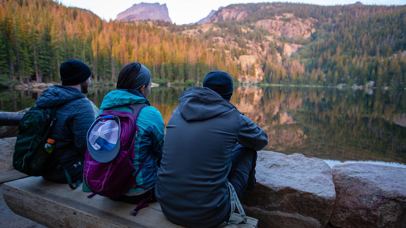 three people sit at the edge of a lake and enjoy the view