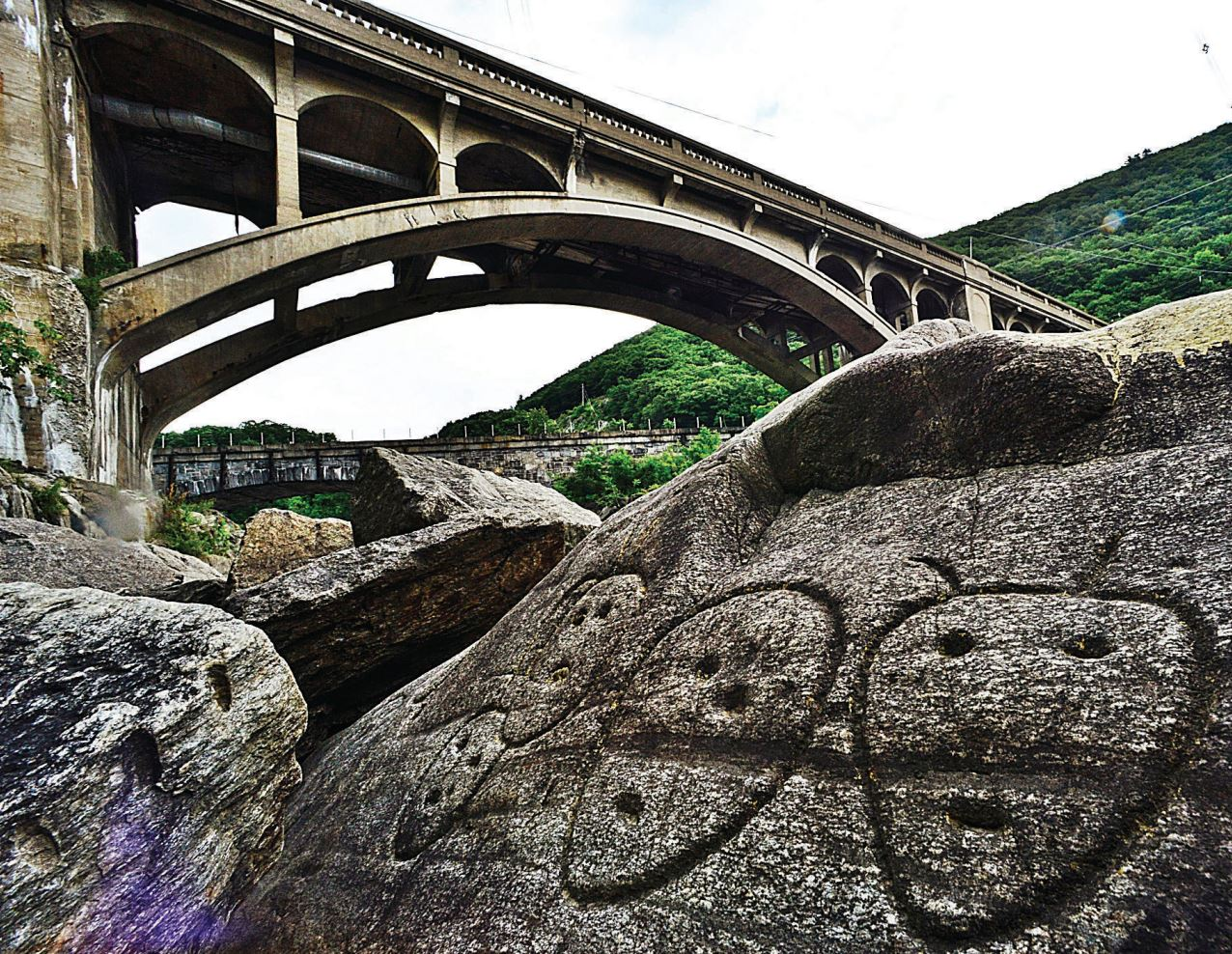 Rocks with carvings on them in foreground; bridge in background