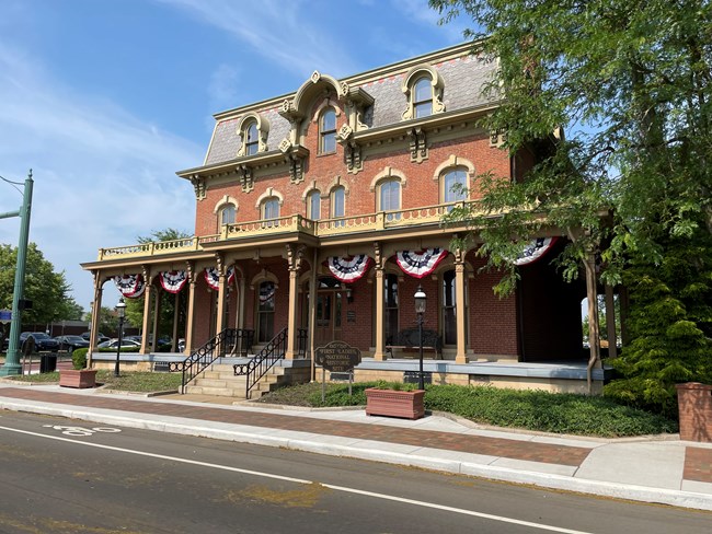 Front of the Saxton House with red, white, and blue bunting between the 8 pillars on the front porch and a brown metal sign with gold words First Ladies National Historic Site.