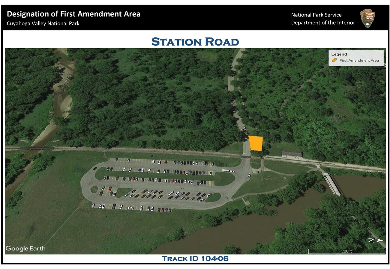 Aerial view of the Station Road area; at center is the Station Road parking lot, its driveway entering from the west; west of the railroad tracks and north of the driveway a trapezoidal yellow polygon indicates the location of the first amendment area.