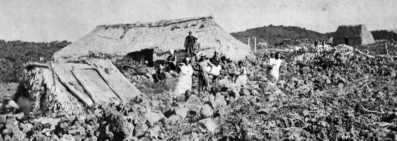 A broken structure in a lava field with people in the foreground