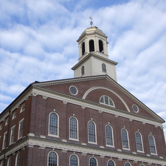 Large brick building with lots of windows and a white copula. White trim surrounds each window.  