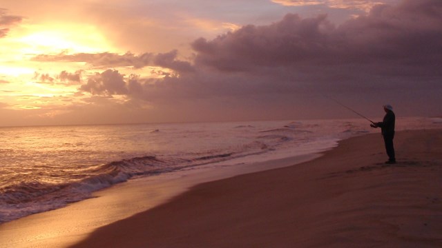 An angler on the beach at sunset