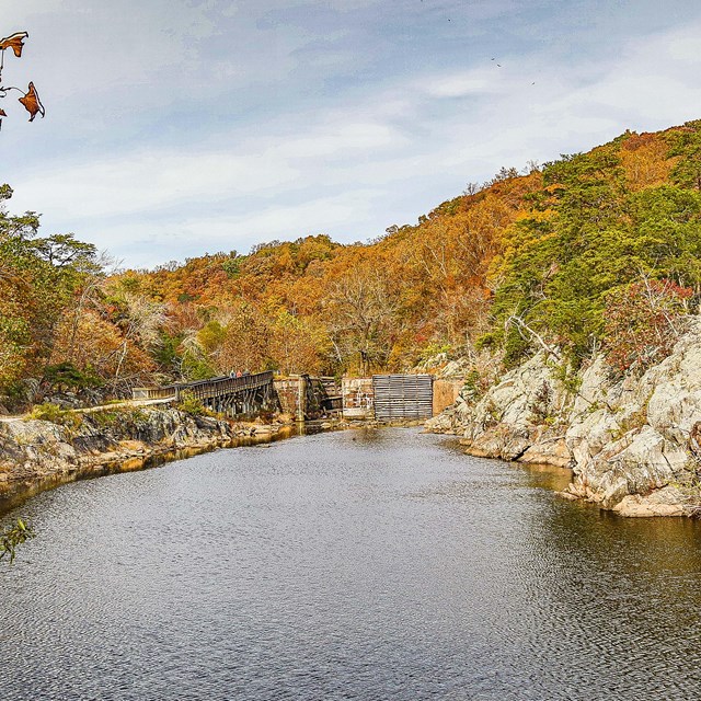 A rock wall and the towpath frame the canal leading to a large lock.