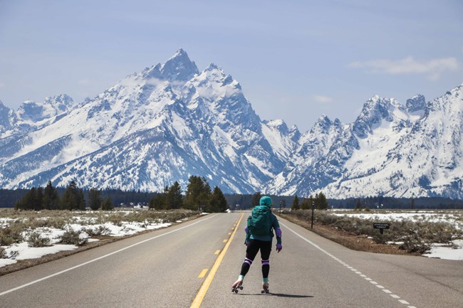 Visitor skates toward the snow covered Teton Range on the Teton Park Road