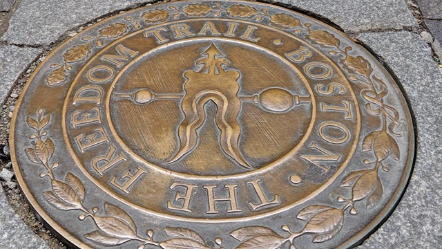 A circular bronze plaque reading "The Freedom Trail" points visitors to the red lined path.