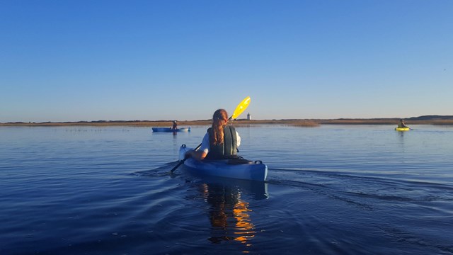 A ranger pulls a canoe down a ramp towards a pond, as a mother and son follow holding paddles.