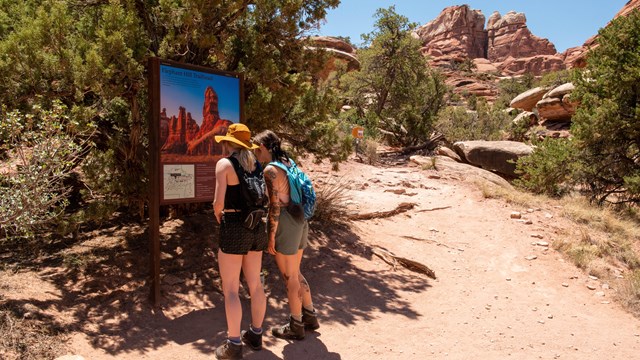 Two hikers read a trailhead sign before beginning their hike