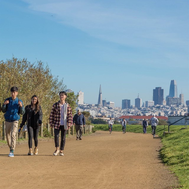 people walking along a wide gravel path at Crissy Field with San Francisco skyline behind