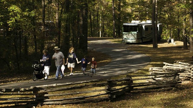 a family walks along the park road with their RV in the distance.