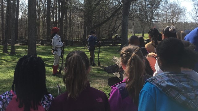 Students gather around a historic weapons demonstration.