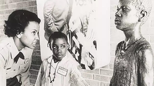 Historic photo of a ranger talking to a kid at a statue of Booker T. Washington as a kid