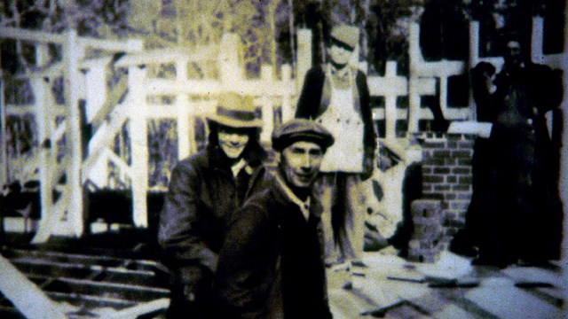 4 men stand in a partially constructed cabin of wood and brick