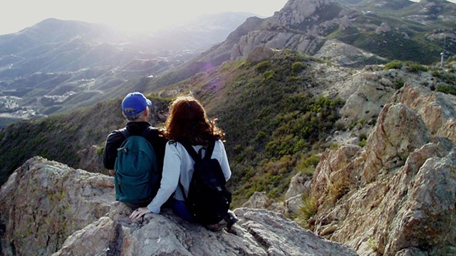 Two individuals sitting atop a rocky outcrop while watching the sunset.