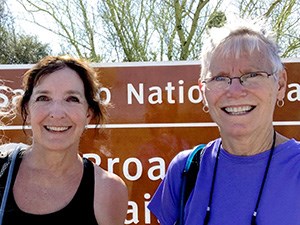 Two smiling women stand in front of a national park sign