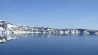snow covered caldera walls run horizontally between a cloudless blue sky and a deep blue lake