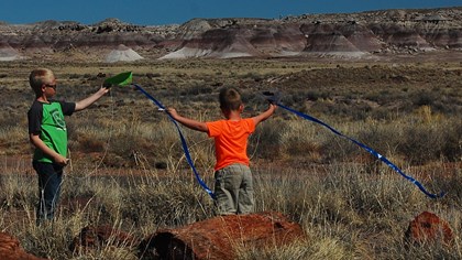 children with outstretched arms fly kites against the backdrop of striped badlands buttes.
